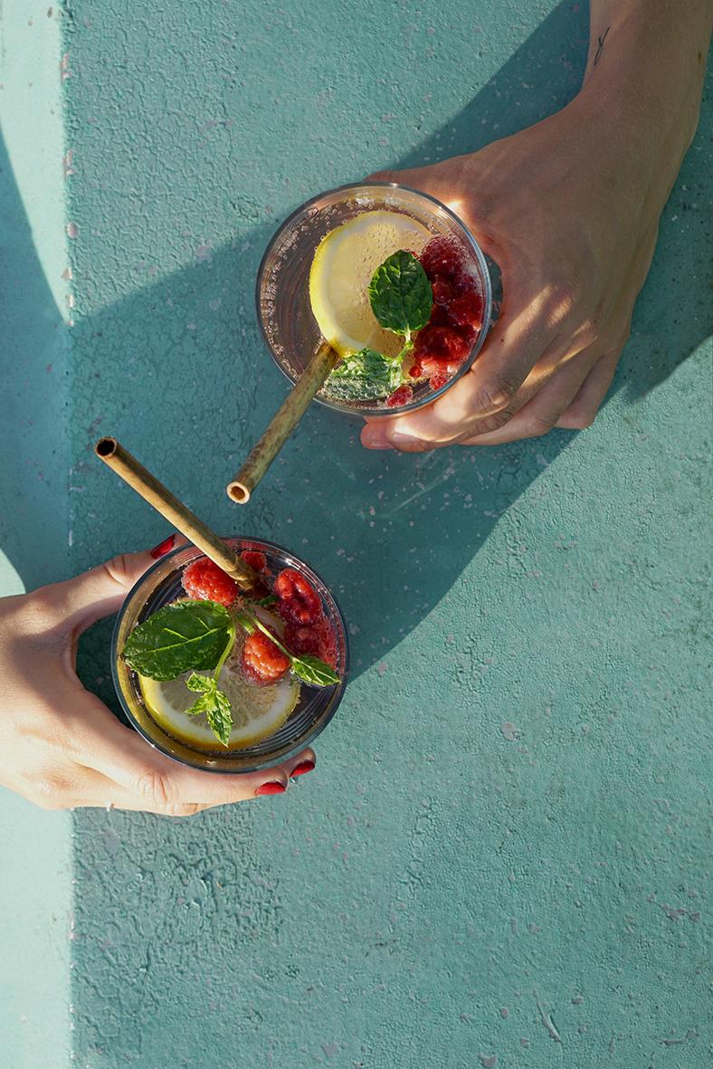 Två glas med citron, jordgubbar och mynta på en blå yta, ett av glasen har ett sugrör