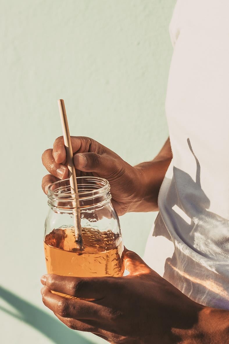 Person som håller ett glas med honung och ett sugrör, bakgrund i ljusgrön nyans