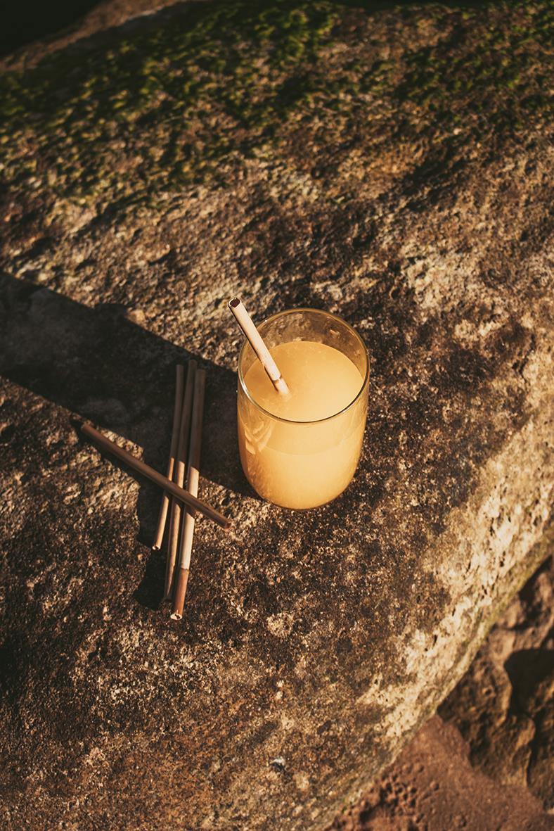 Glass med gul dryck och sugrör på stenig yta med skuggor och naturligt ljus