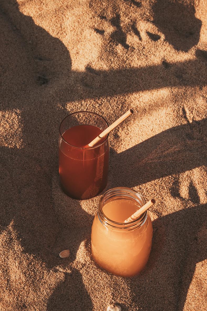 Två drycker i glas och en burk med sugrör på sandstrand, solskugga