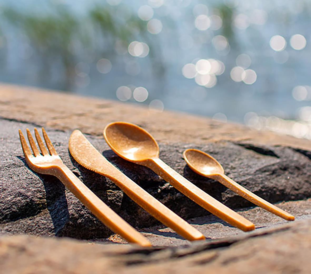 Flergångs kaffesked i brunt biokompositmaterial på en träyta med vatten och ljusreflexer i bakgrunden