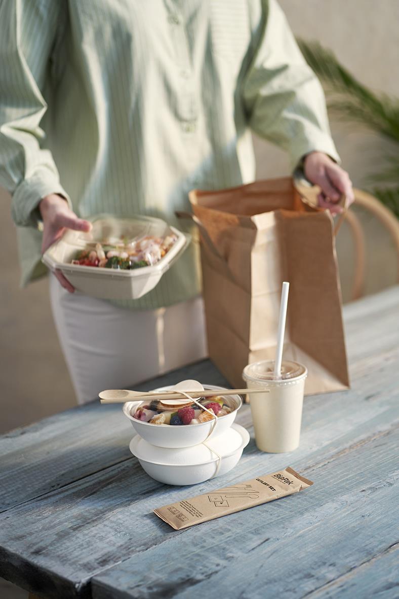 Person som packar en pappersmugg med mat och dryck på ett bord, med en papperspåse i bakgrunden