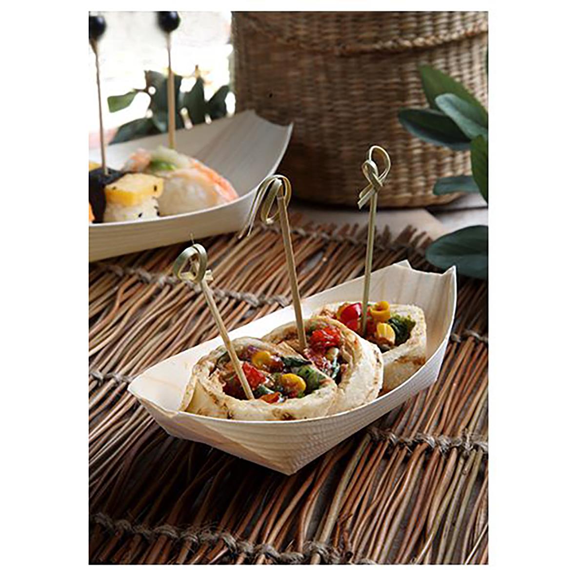 Skål med små mackor eller tapas på en träbåtformad skål med pinne, på ett bambutäckt bord