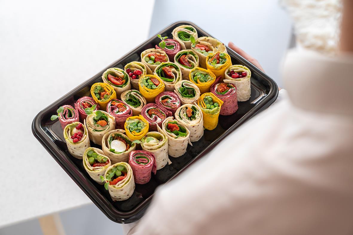 Serveringsfat med rullade smörgåsar i olika färger på svart uppläggningsfat