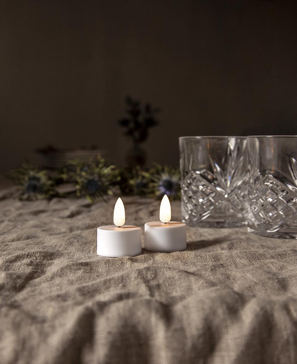 Två LED-värmeljus med flammor bredvid kristallglas på ett bord