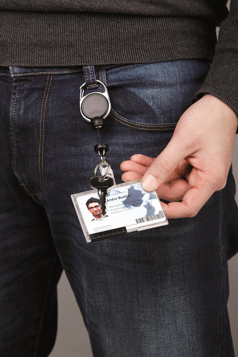 Person håller i ett ID-kort med svart klädsel och jeans, ID-lanyard hänger från midjan