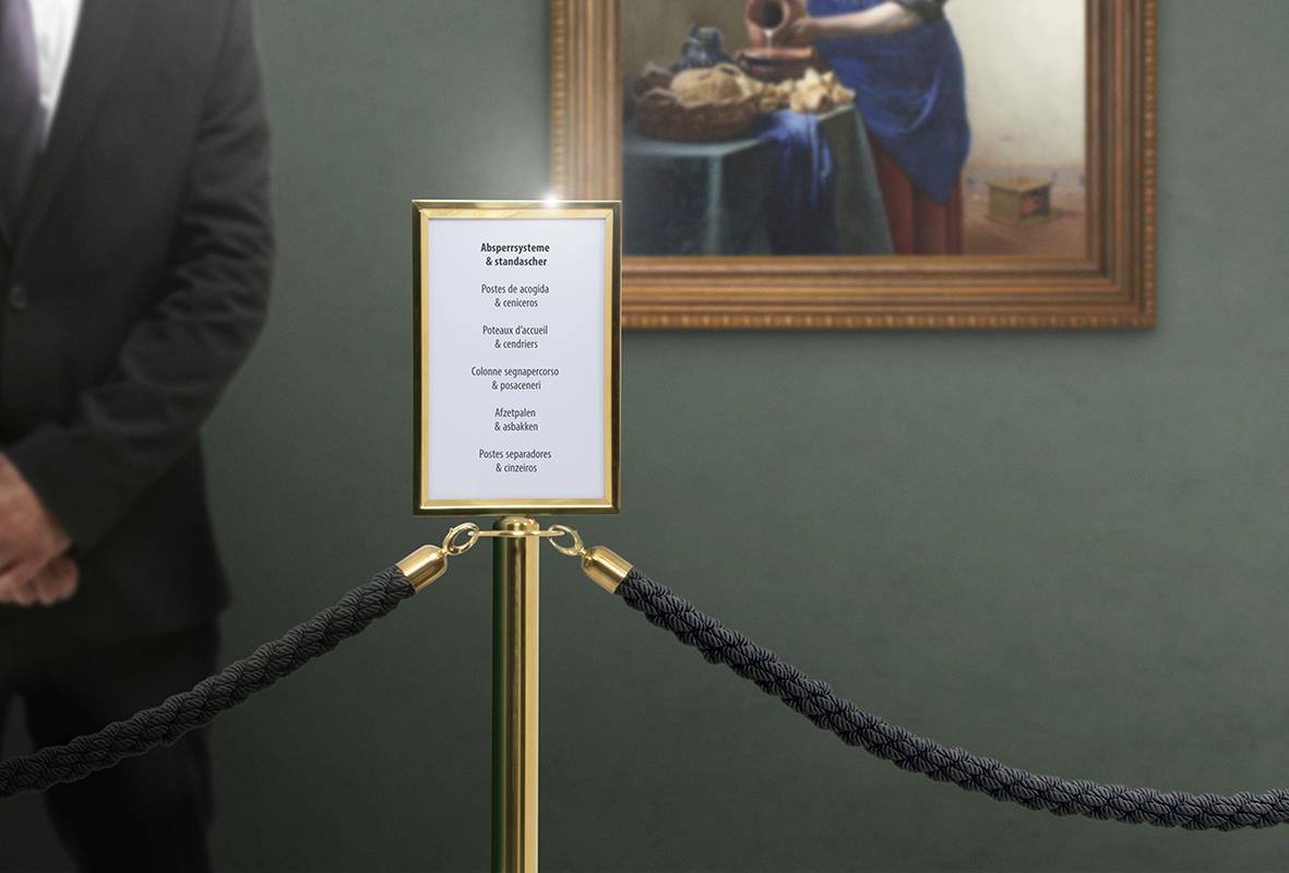 Guldfärgad avspärrningsskylt med text, placerad mellan två staket i ett konstgalleri