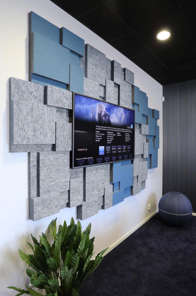 Ljudabsorberande väggpaneler i blå och grått, monterade runt en TV, i ett modernt rum med växt och sittmöbel