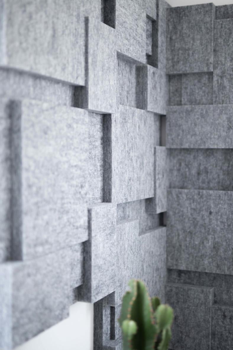 Blå ljudabsorberande paneler i nivå 3-pack på vägg med en liten växt i förgrunden