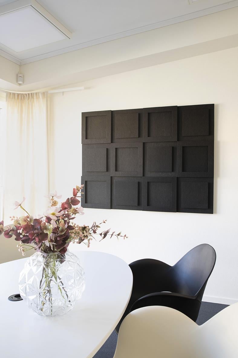 Ljudabsorberande svart väggpanel i modern design på vit vägg i rum med blomsterarrangemang