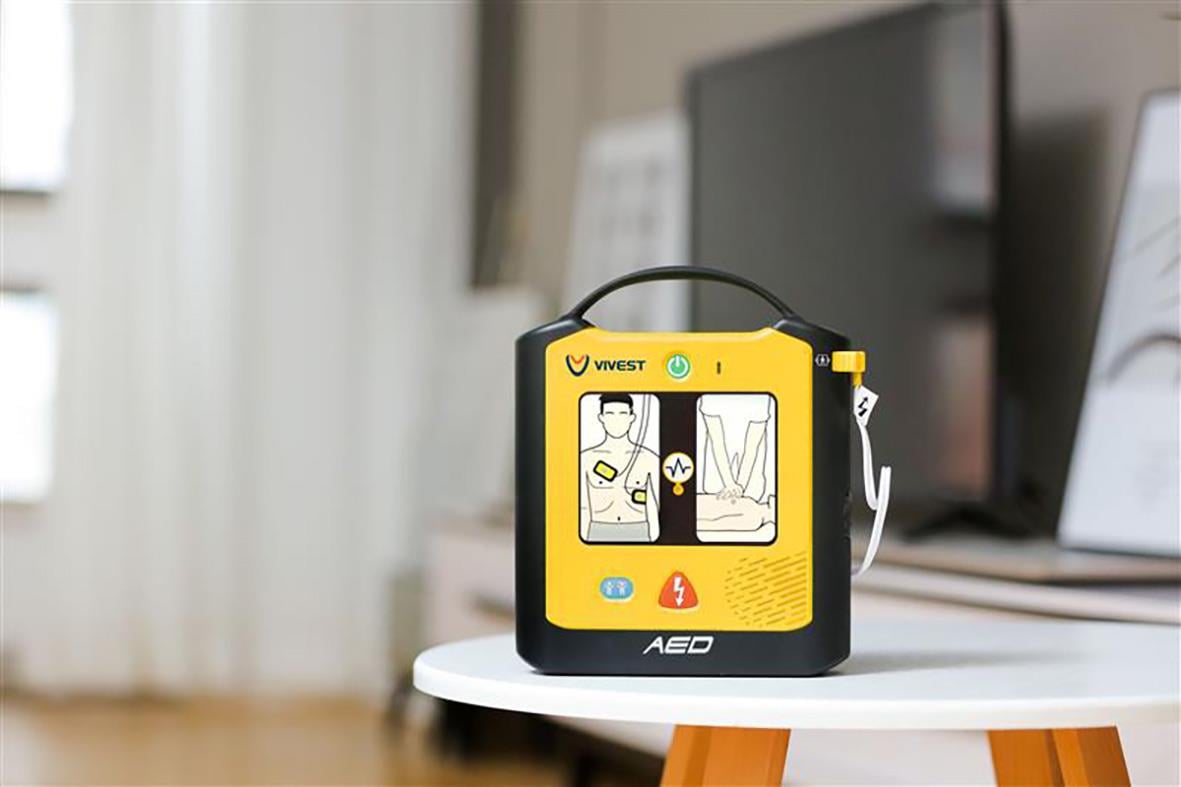 Hjärtstartare ViVest Serie 1 i gul färg placerad på ett runt bord i ett inomhusmiljö
