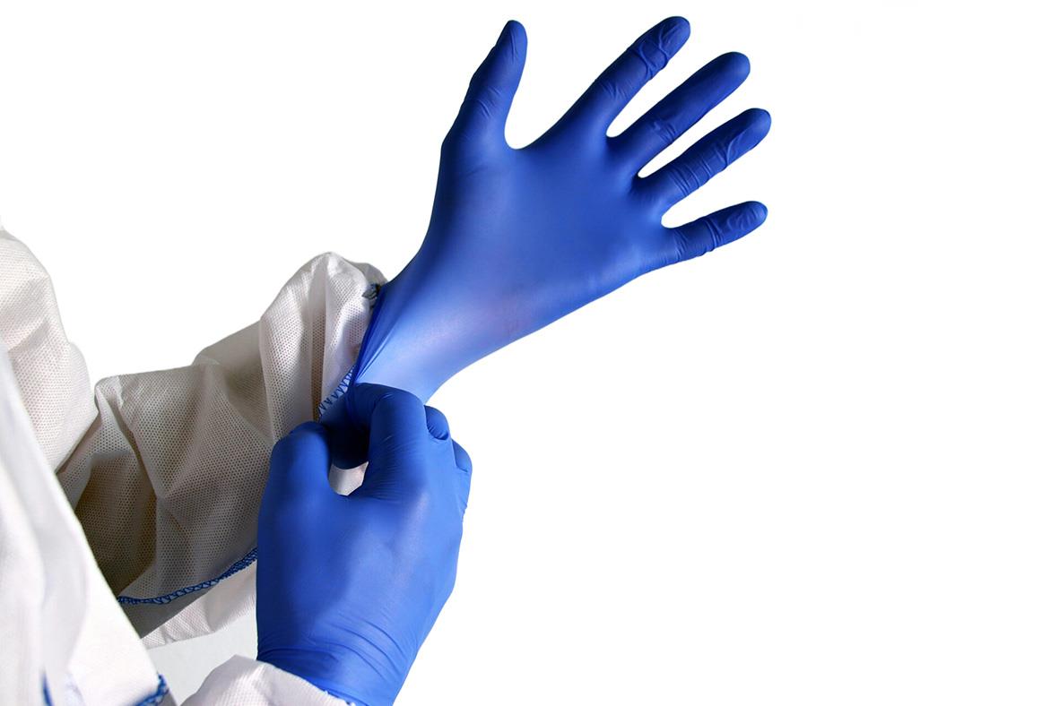 Person som sätter på sig blå medicinska handskar, del av vit skyddsoverall synlig