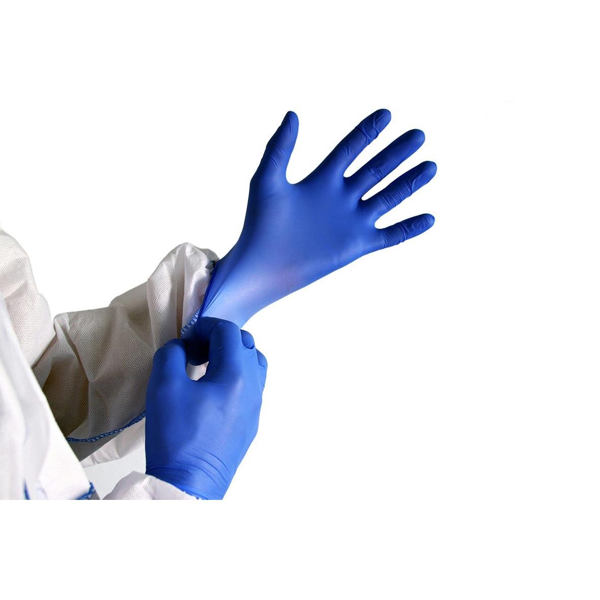 Person som sätter på sig blå medicinska handskar, del av vit skyddsoverall synlig