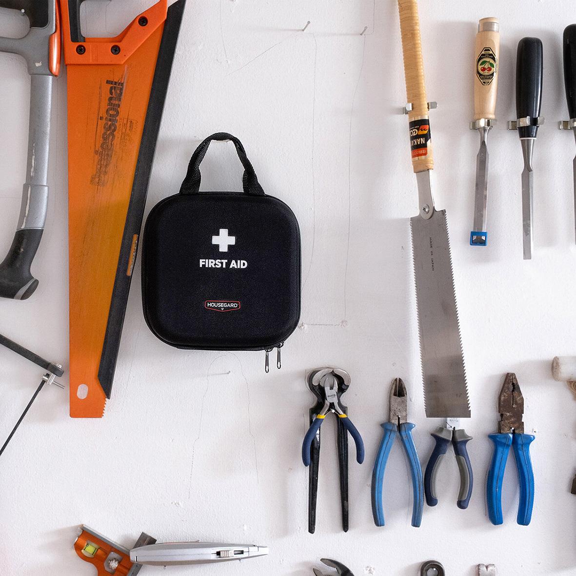 Första hjälpen-kit Housegard Standard omgiven av verktyg och verktygssatser på en vit yta