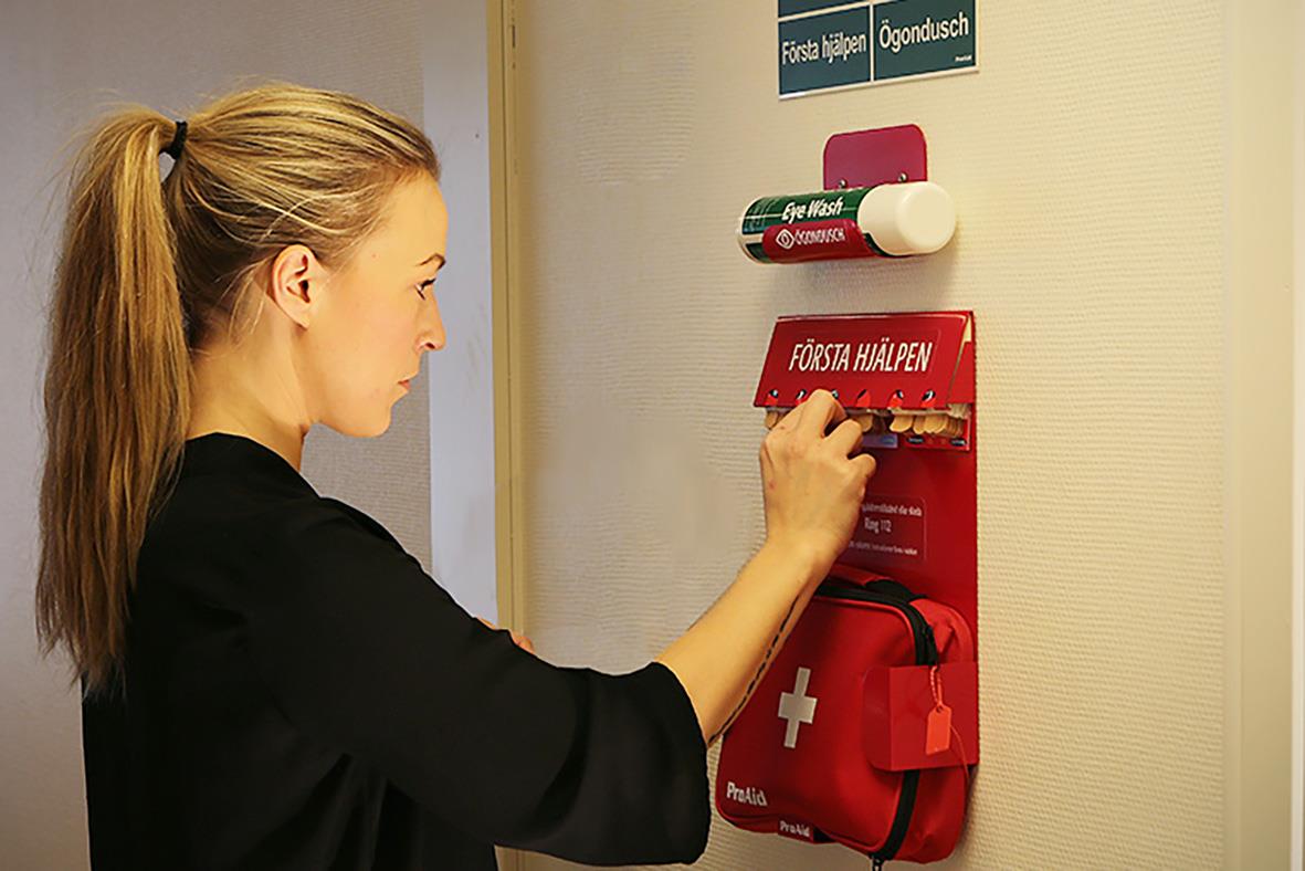 Kvinna hämtar förbandslåda från väggmonterad första hjälpen station på kontor eller hem