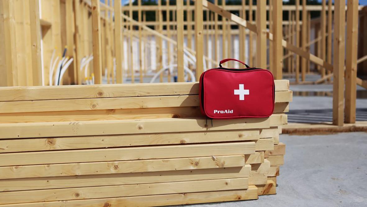 Röd Första Hjälpen väska från ProAid placerad på träbalkar i industri- eller lagermiljö
