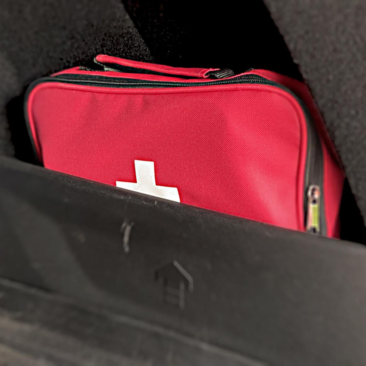 Röd Första Hjälpen väska med vit korssymbol i bilens förvaringsutrymme
