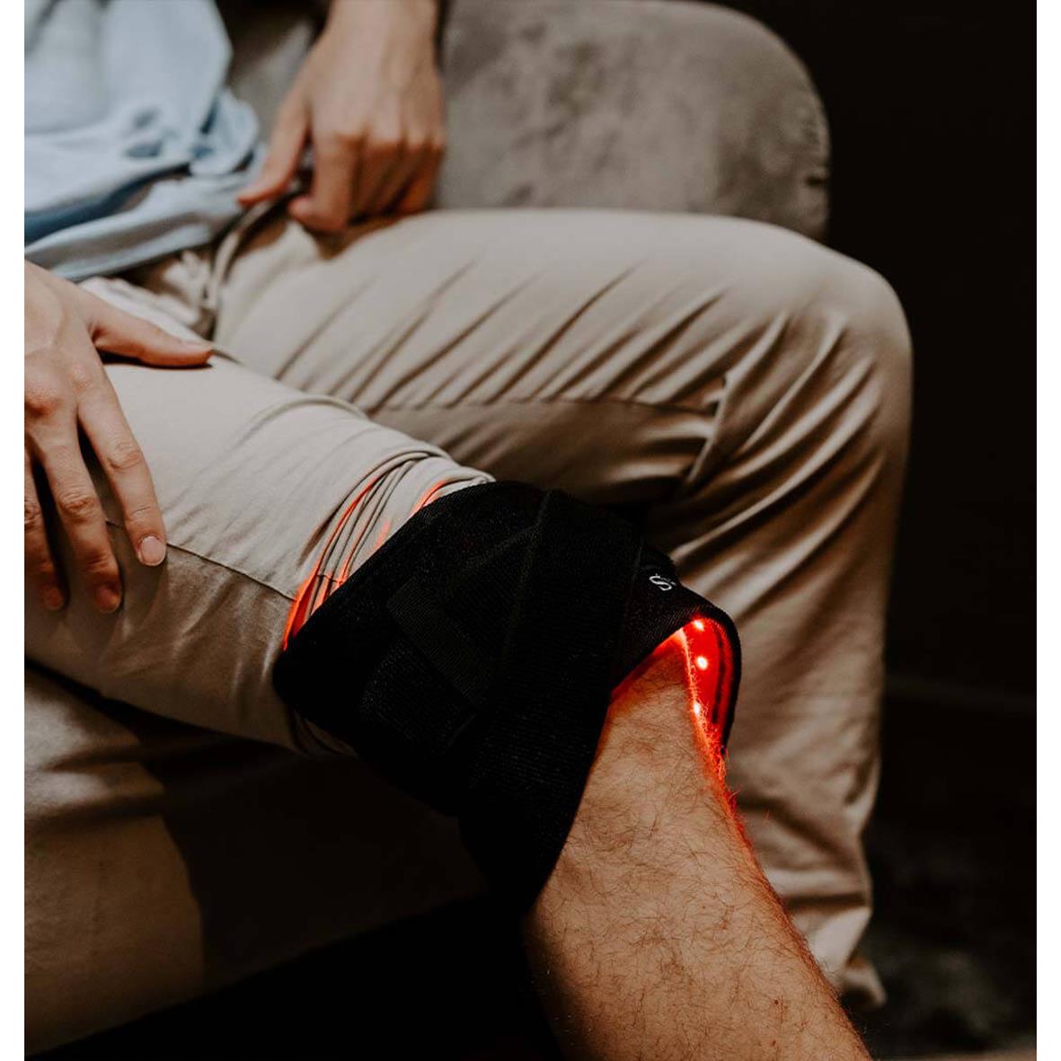 Person som bär ett infrarött ljusbälte på knät, sittande på en soffa