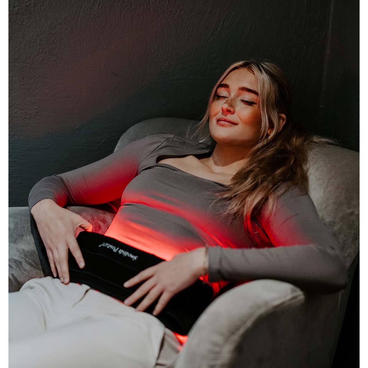 Kvinna ligger bekvämt på en soffa med Bälte InfraEaz Swedish Posture med infrarött ljus, som ger en lugnande effekt