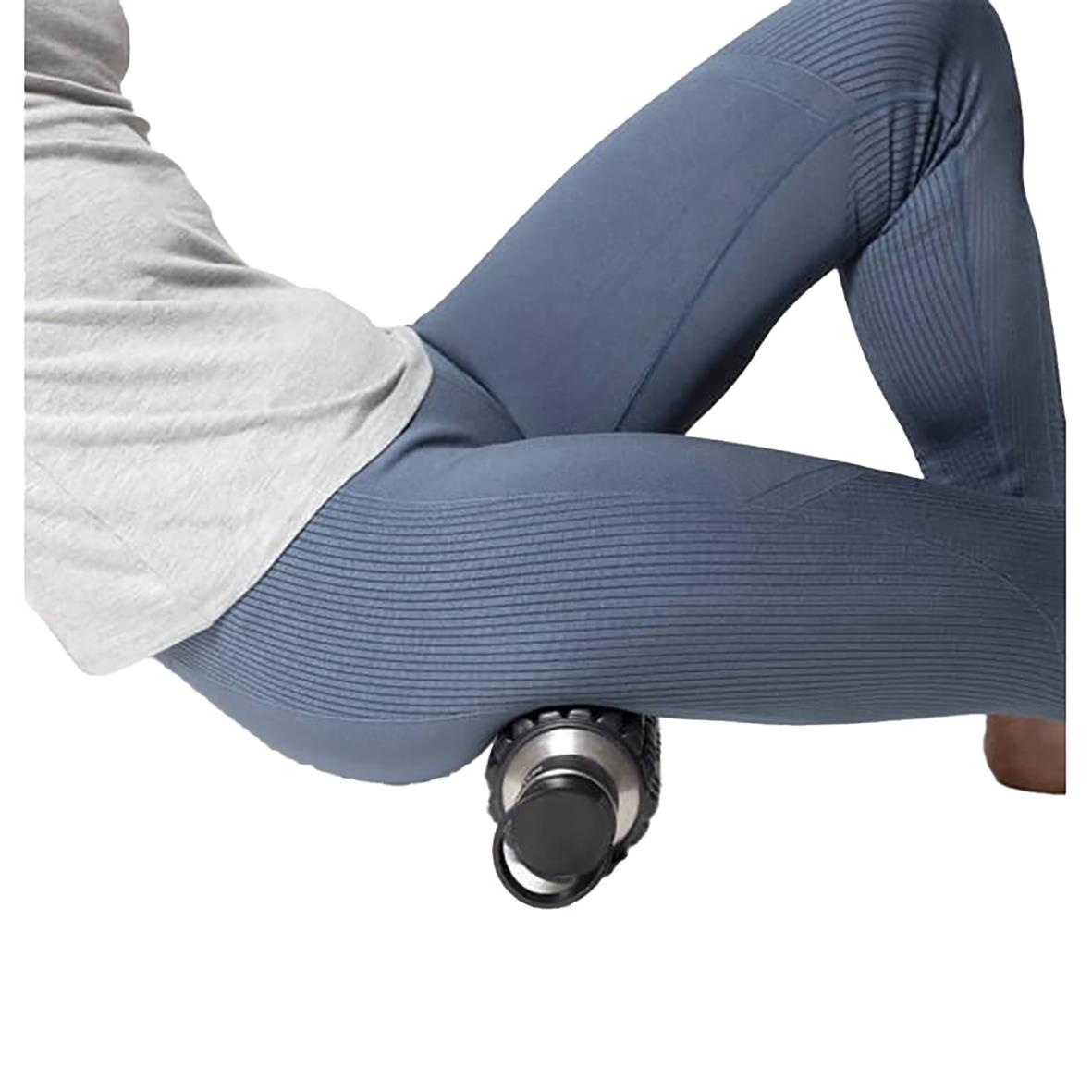 Person använder en foam roller under låret för muskelmassage, med vattenflaska och träningskläder