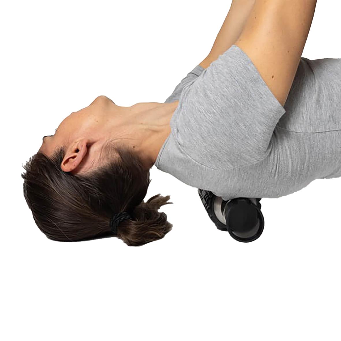 Kvinna som använder en foam roller för ryggmassage, klädd i grå t-shirt, liggande på golvet