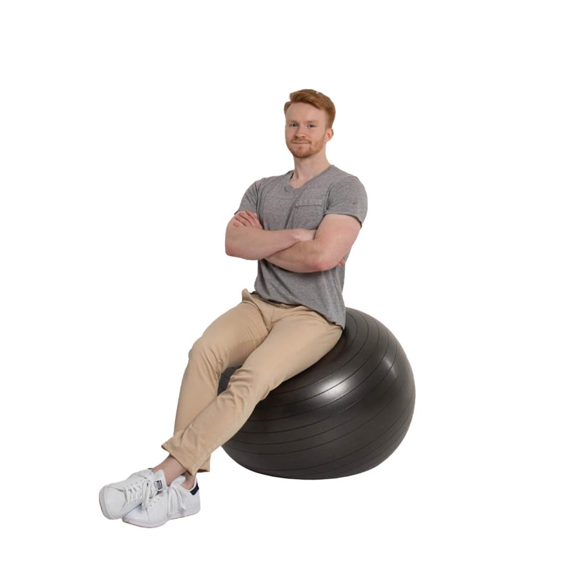 Man sitter på en stor svart gymboll med träningsband, korslagda armar, i en inomhusmiljö