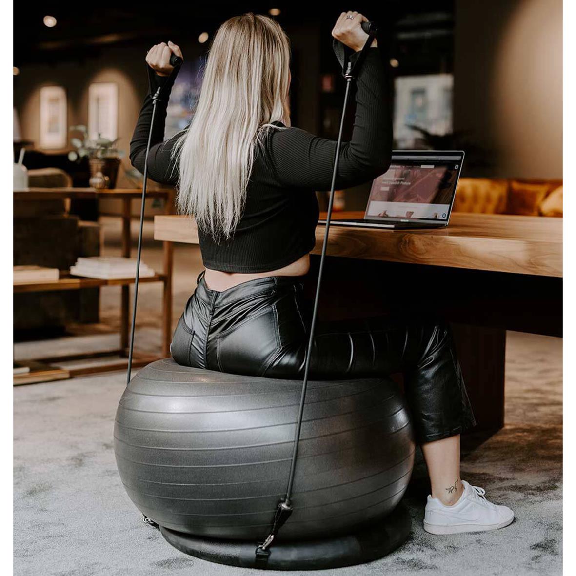 Kvinna tränar med gymboll och träningsband i ett modernt inomhusmiljö