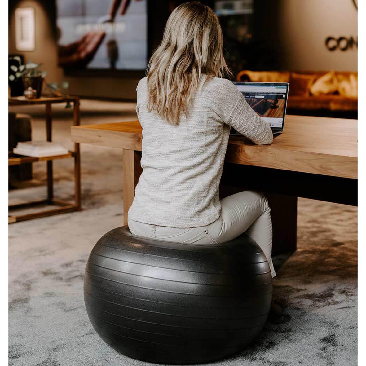 Kvinna sitter på träningsboll framför en dator i ett vardagsrum