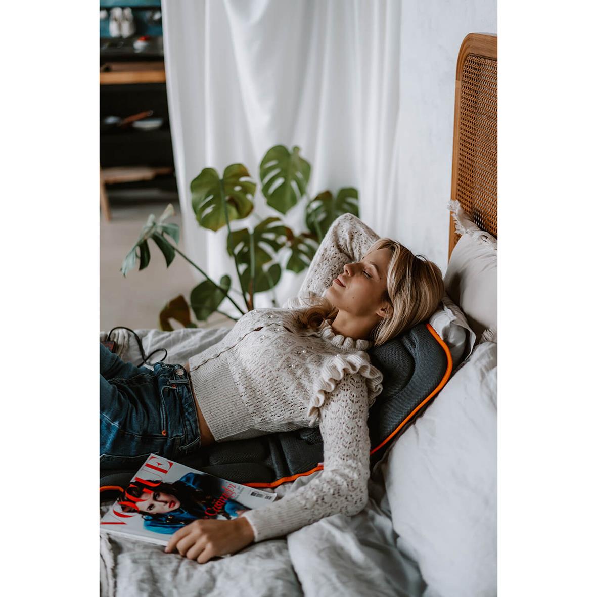 Kvinna ligger på massagematta Medivon Cosy Vibra i sängen och läser en tidning