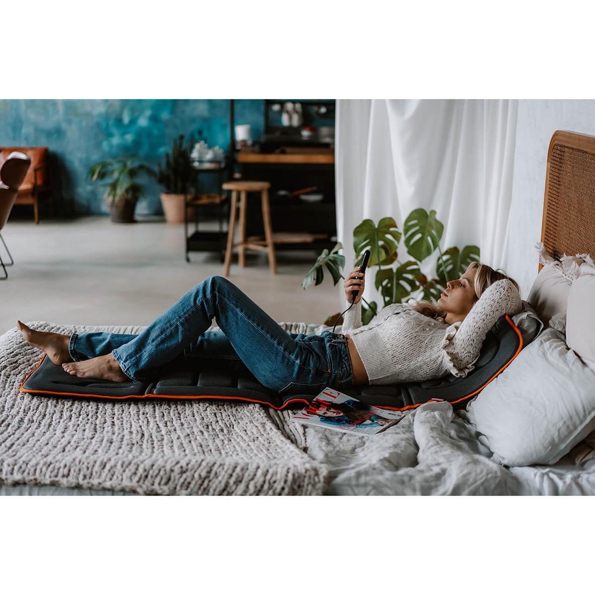 Person som vilar på en massagematta Medivon Cosy Vibra i ett mysigt hem med växter och inredning
