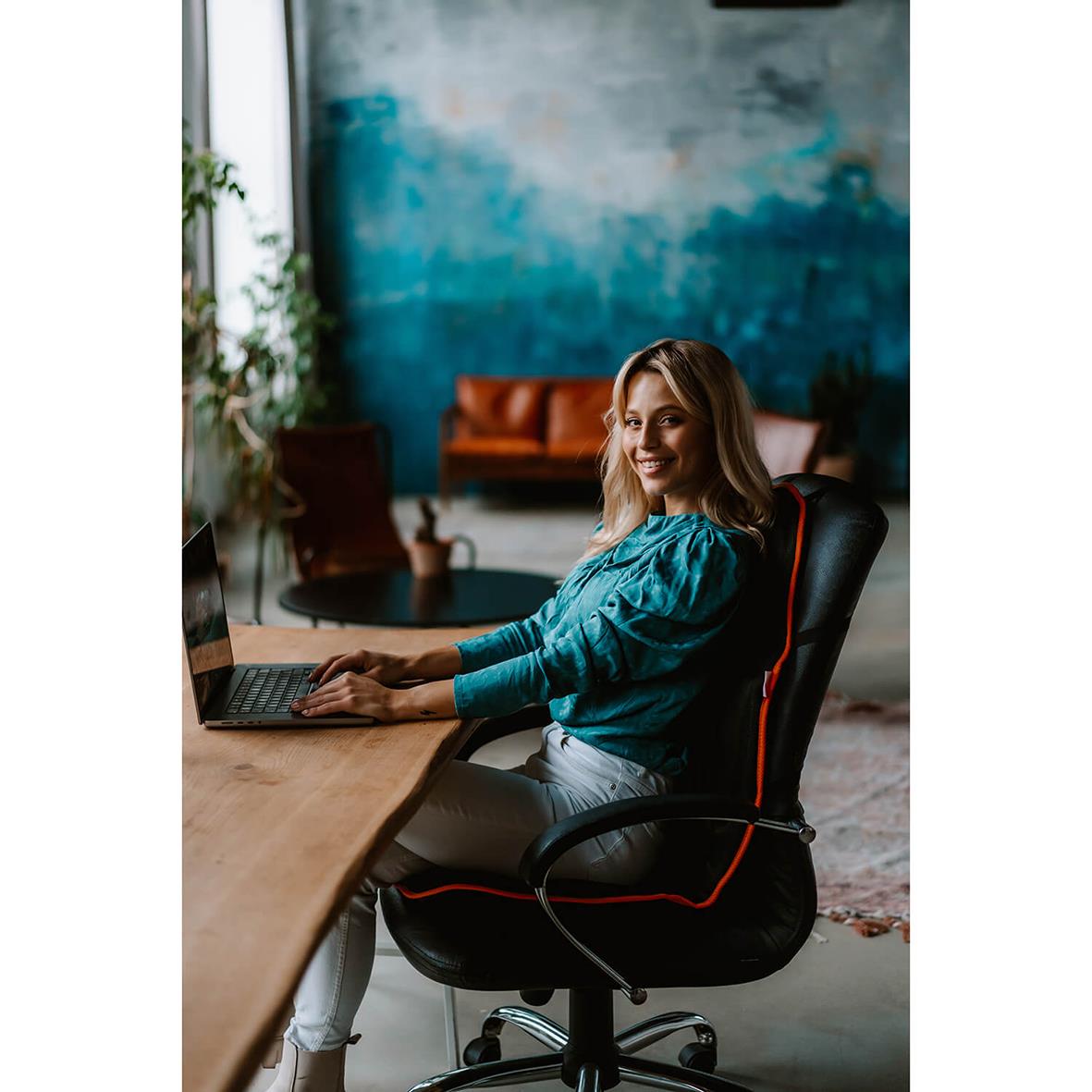 Kvinna sitter vid skrivbord med laptop i ett modernt kontor, ler och ser nöjd ut