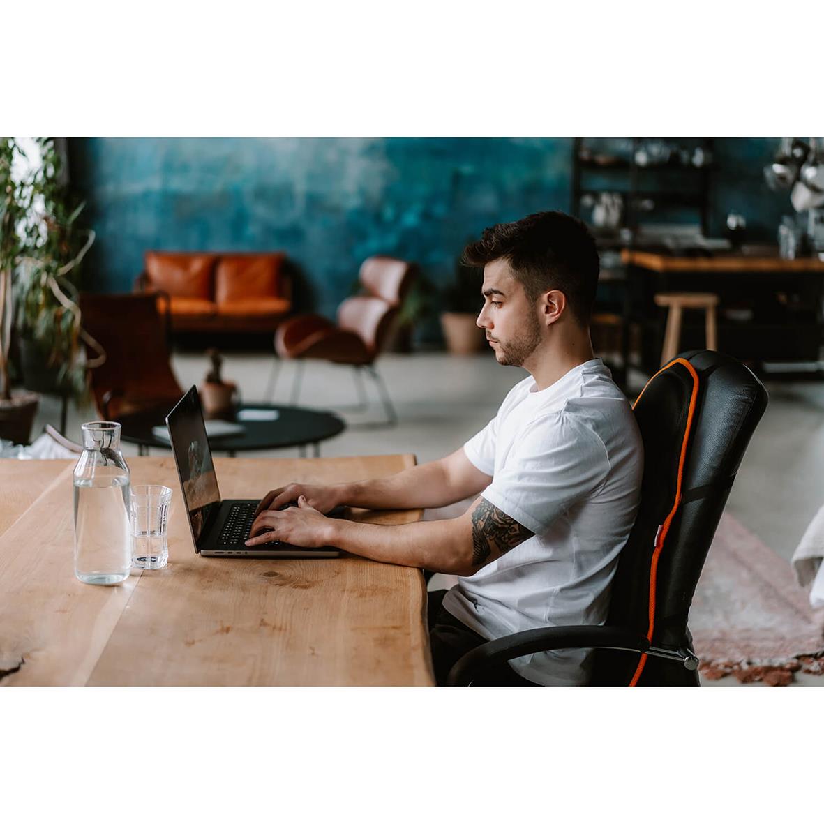 Man arbetar vid ett bord med laptop i ett modernt kontorsutrymme med gröna väggar och soffor i bakgrunden