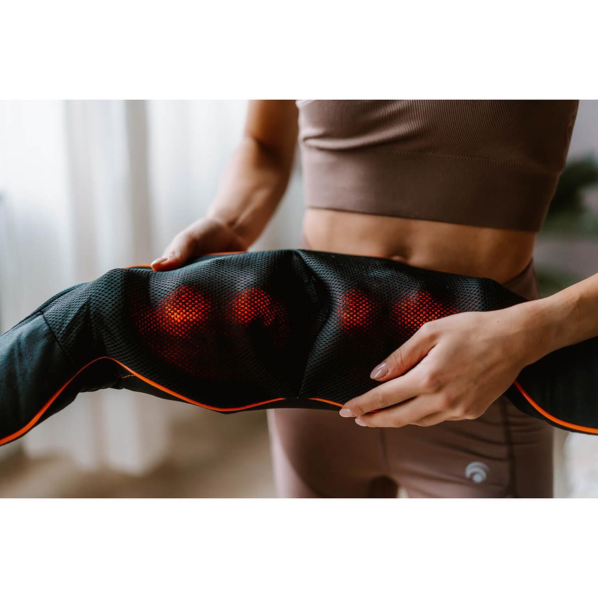 Person som använder en svart nackmassageapparat med röda ljus på lår och mage