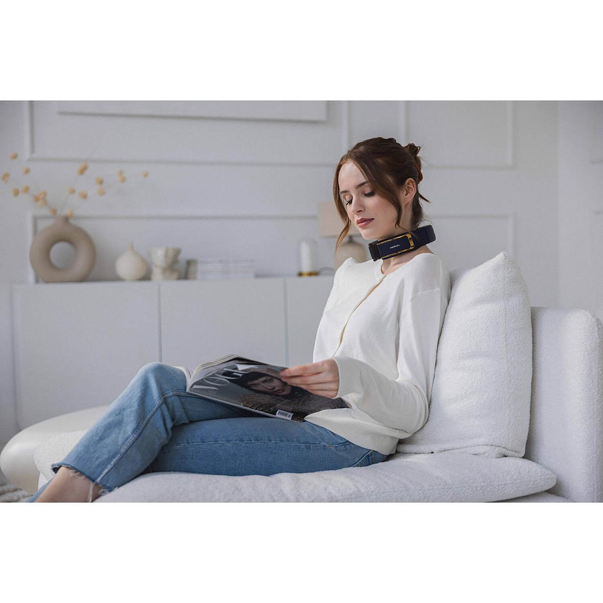 Kvinna använder nackmassageapparat Medivon Ultra EMS Pro sittande på en soffa i ett modernt hem