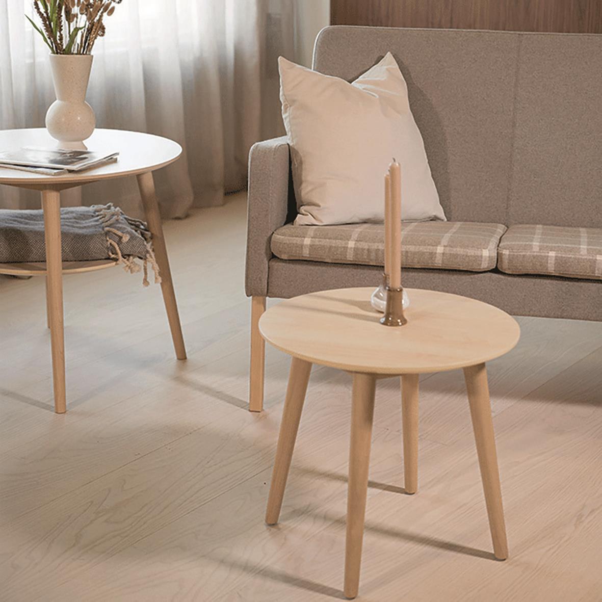 Vardagsrum med soffa, kudde, runt bord med ljus och växt i vas, ljusa färger och naturligt ljus