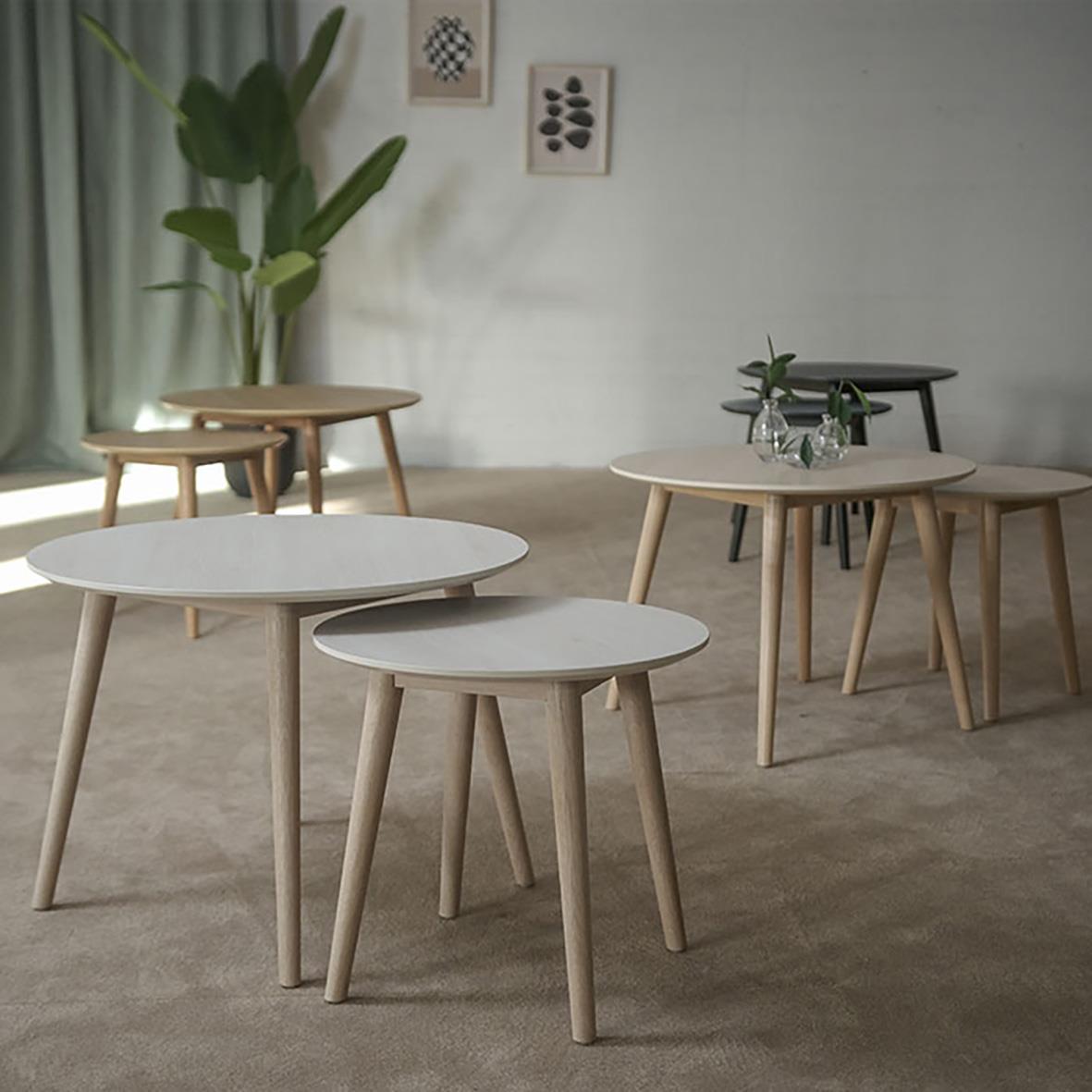 Fyra moderna soffbord i trä och vitt i ett vardagsrum med gröna växter och konst på väggarna