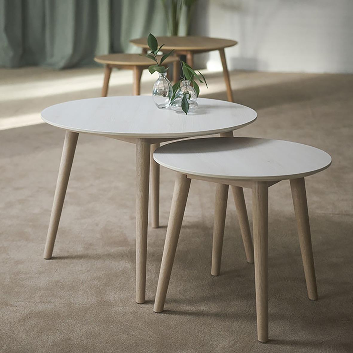 Tre runda soffbord i trä med vita och ljusbruna ytor, placerade på en matta i ett rum med gröna gardiner och ett växtarrangemang