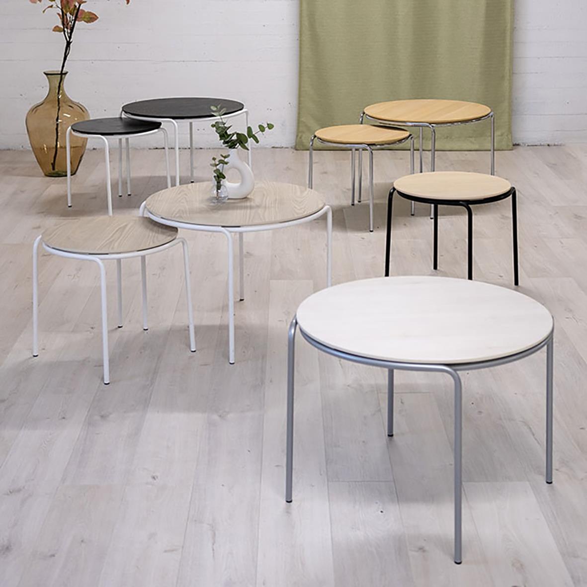 Olika runda soffbord i olika färger och storlekar i ett rum med ljus golv och väggar, samt en växt och en vas i bakgrunden