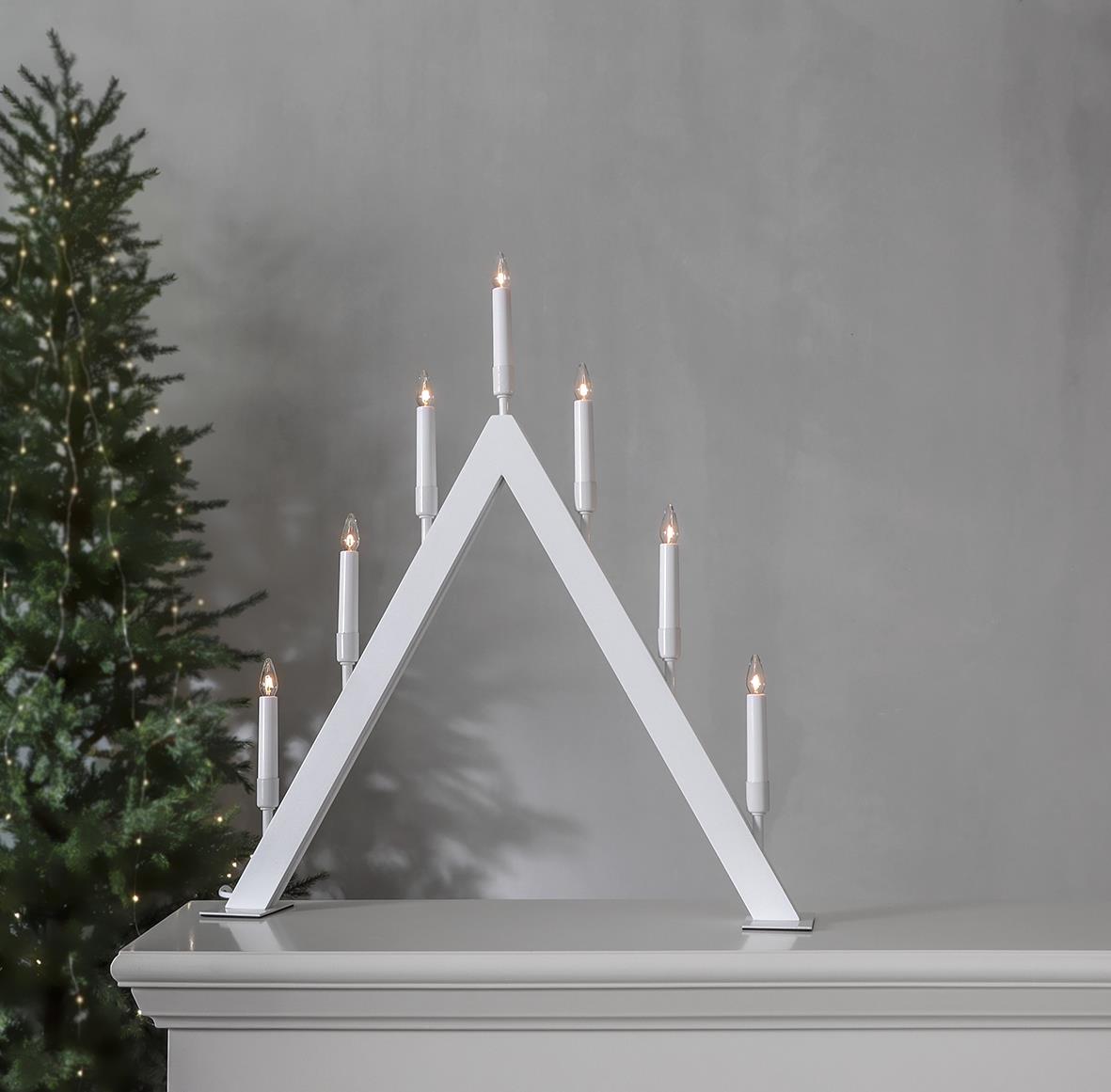 Vit ljusstake i form av ett triangulärt hus med sju ljus, 55,5x63cm, placerad på en vit möbel