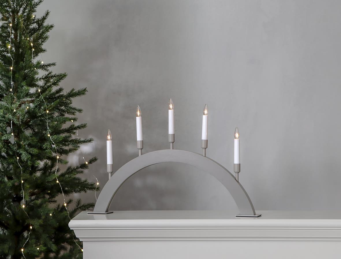 Beige ljusstake i bågform med fem ljus, 57x38cm, placerad på en vit yta framför en julgran