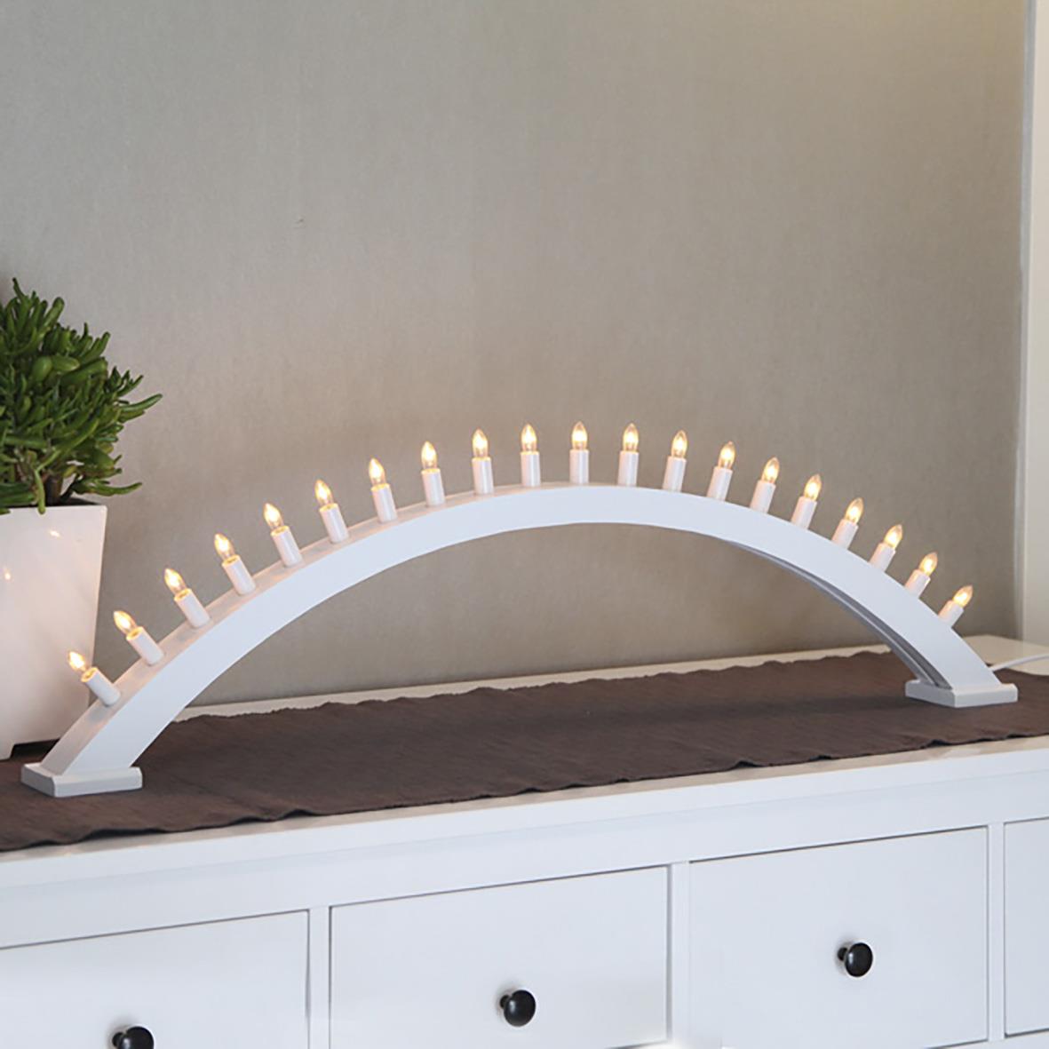 Vit ljusstake i form av en båge med många små ljus på en vit möbel