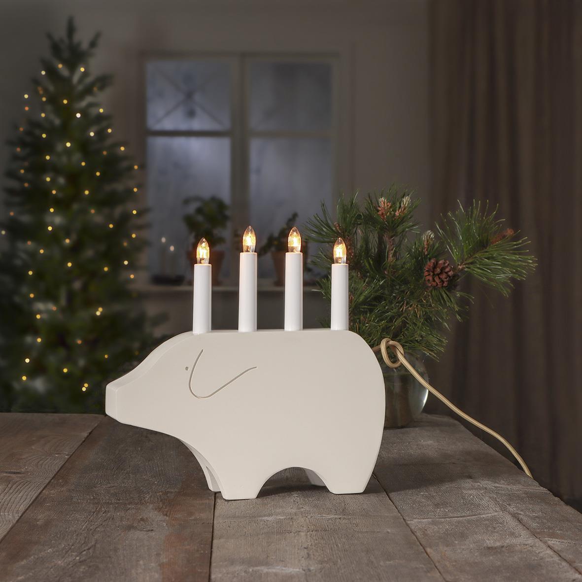 Vit julgris med fyra ljus som ser ut som ett ljusstake, dekorerad med granris