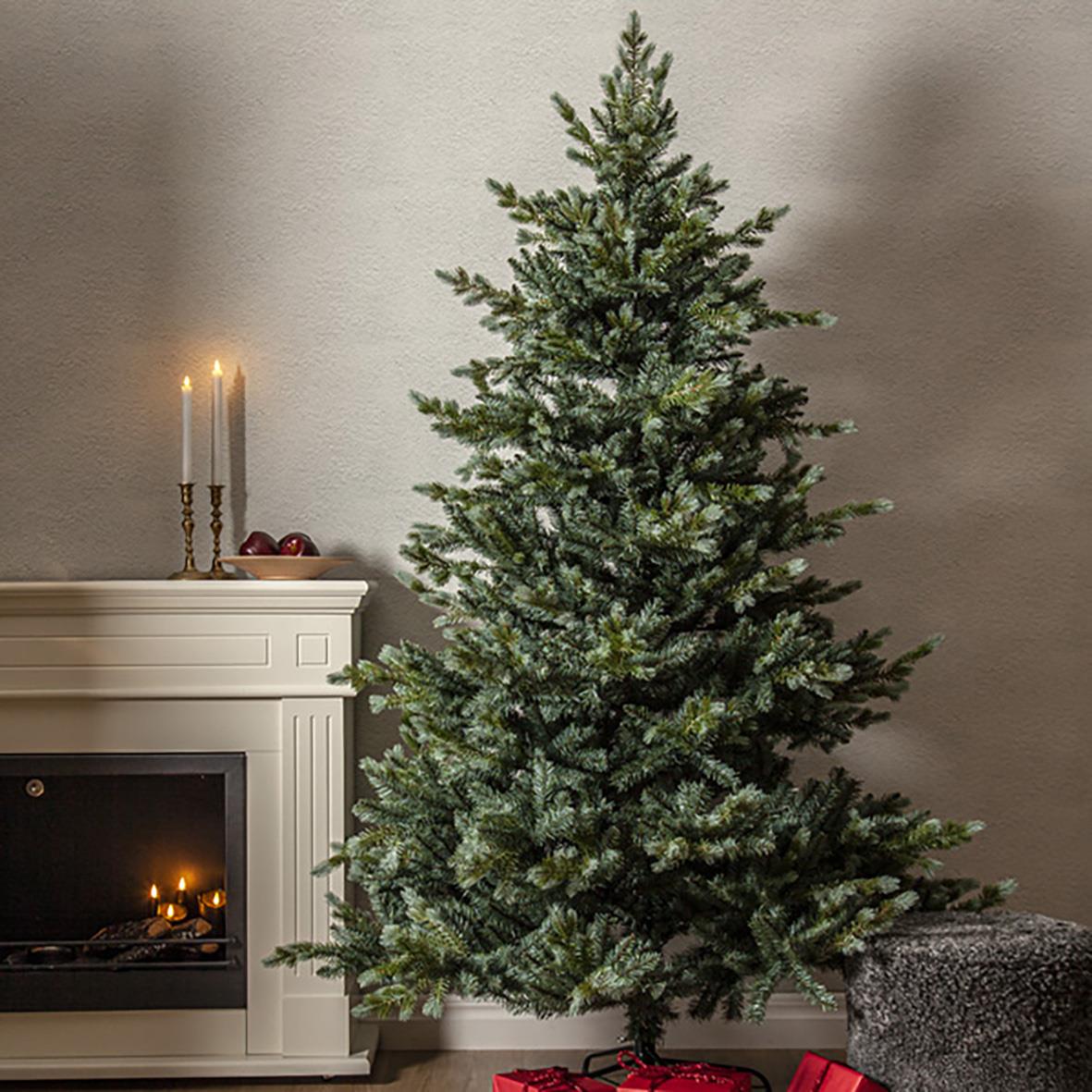 Julgran Greyland 210cm stående framför en vit eldstad med ljus och juldekorationer