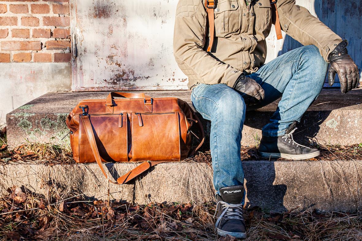 Person sitter på en trappa med en cognacfärgad weekendbag i skinn bredvid sig