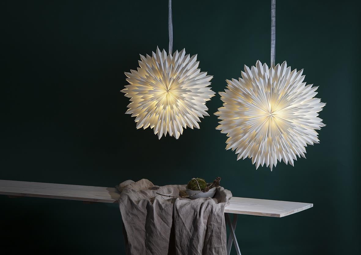 Två julstjärnor i vitt med 70 cm längd hängande mot en mörk vägg