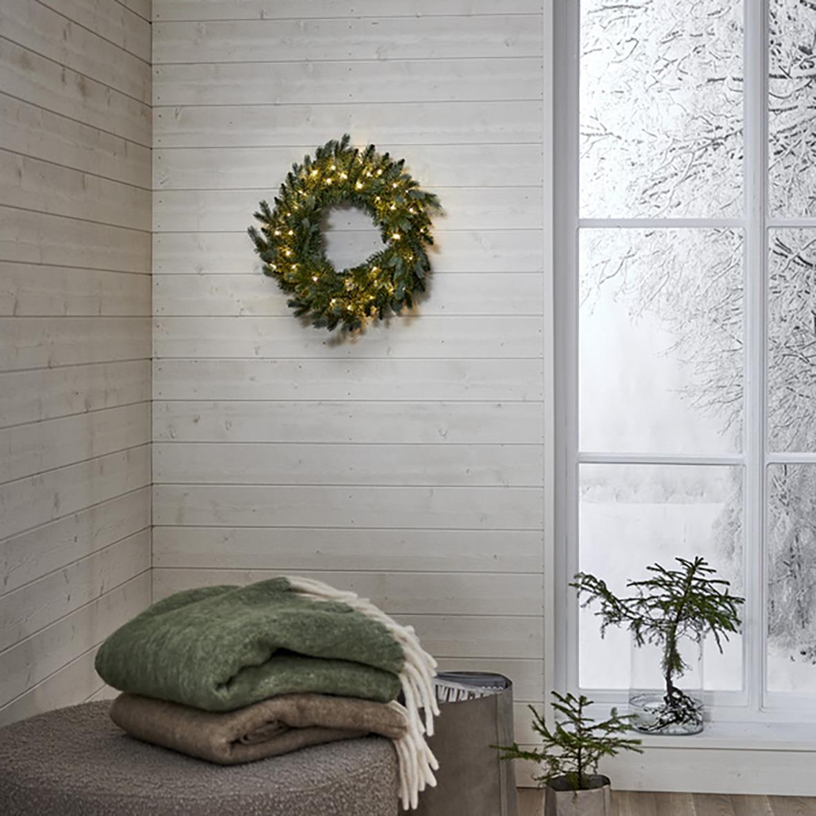 Julkrans med 40 LED-lampor, 55cm, hängande på vit trävägg i ett vinterlandskap