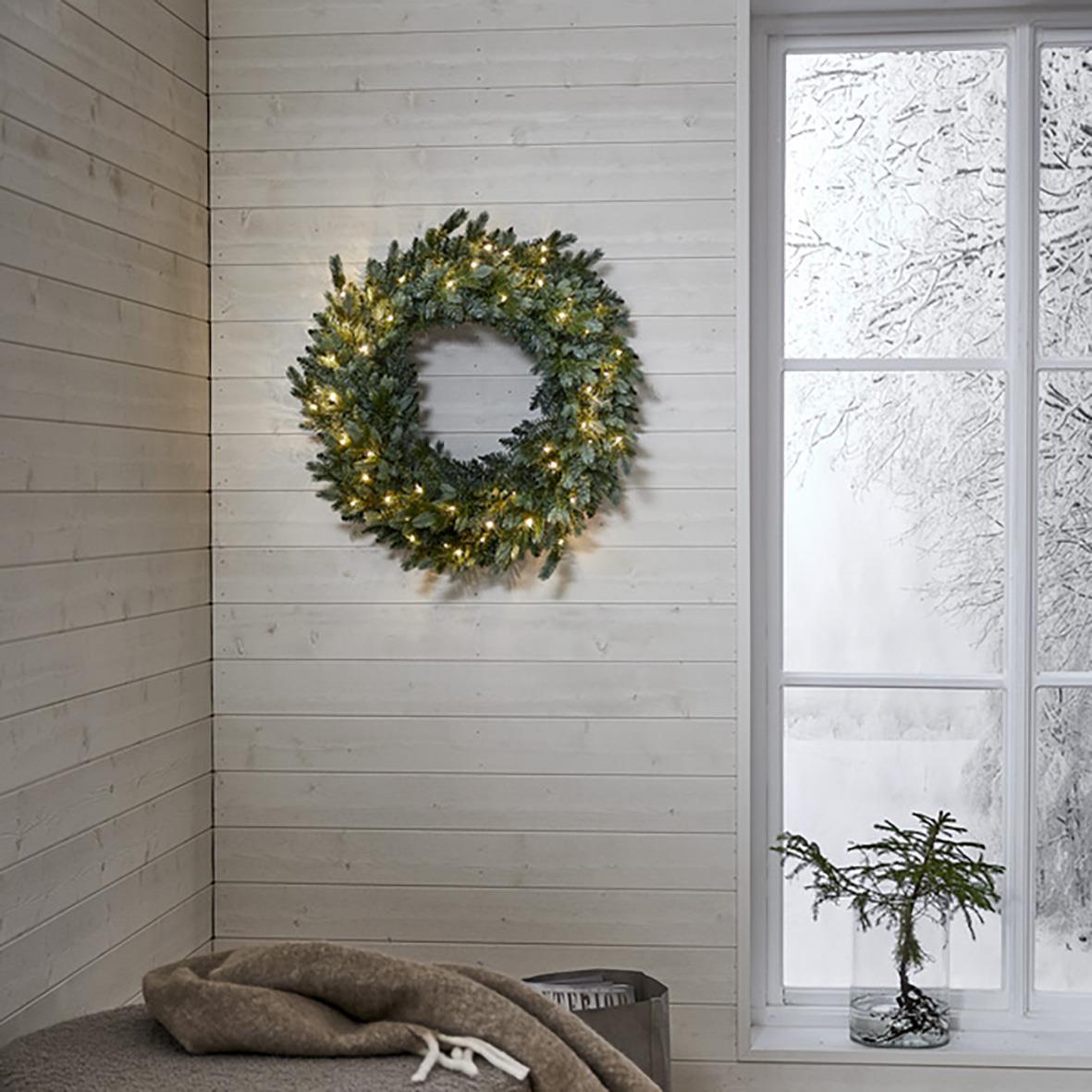 Grön krans med 60 LED-lampor på vit vägg i ett rum med snö utanför fönstret
