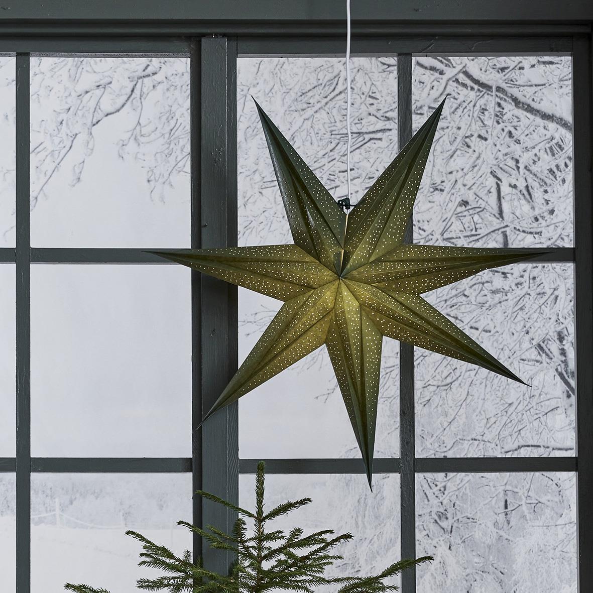Stjärnformad julstjärna hängande framför ett fönster med snöklädd utsikt