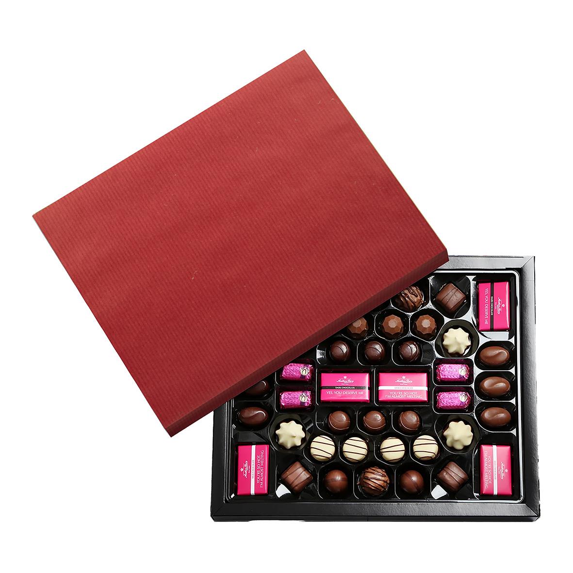 Röd presentkartong med öppnad chokladask med olika chokladpraliner och godisbitar