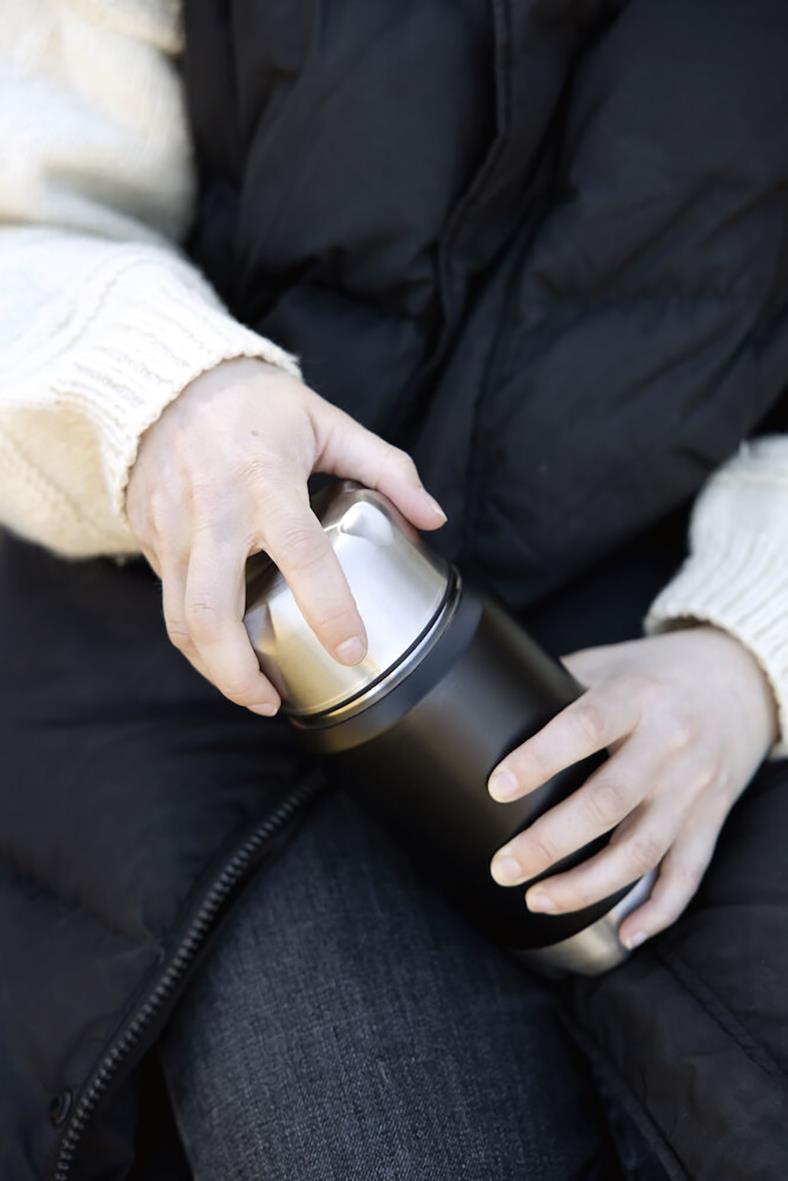 Person håller i en svart termosmugg från Sagaform med 60 cl kapacitet, användbar för varma drycker